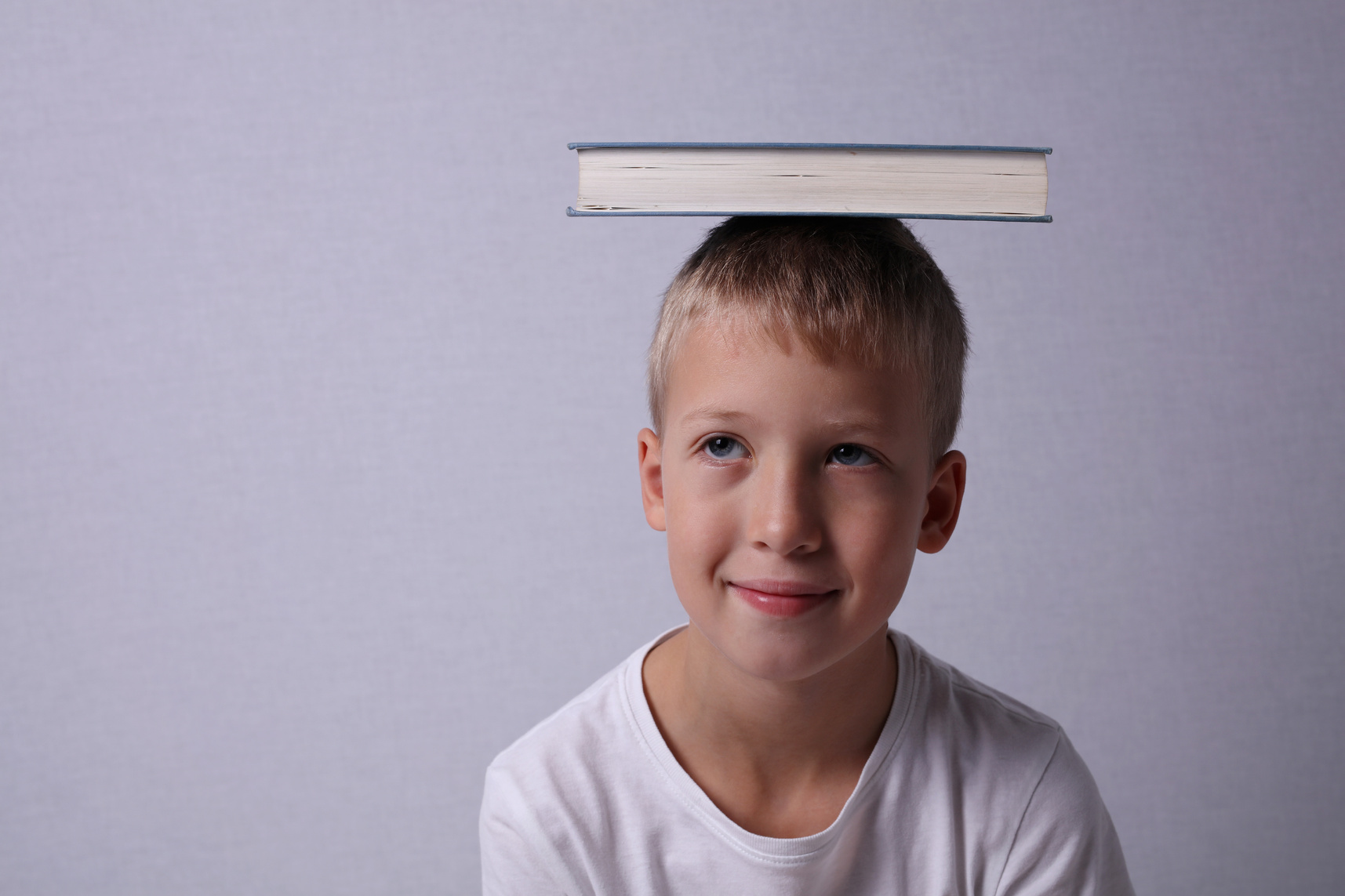 Portrait of smiling School child with book on his head.